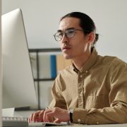 Young Asian male entrepreneur looking at computer screen by workplace