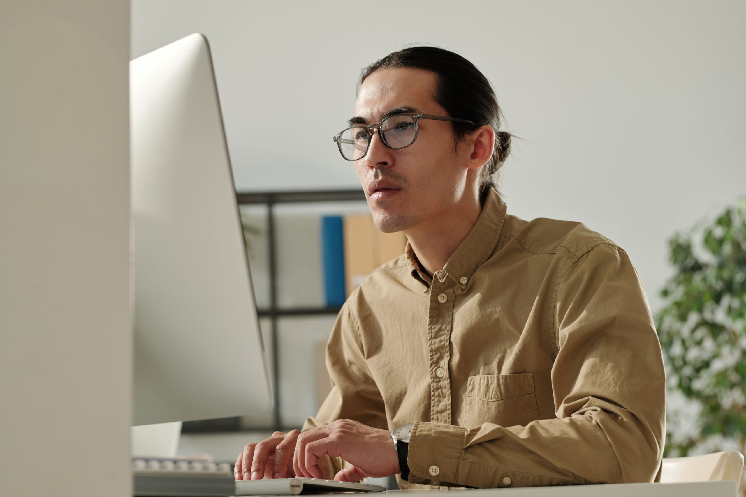Young Asian male entrepreneur looking at computer screen by workplace